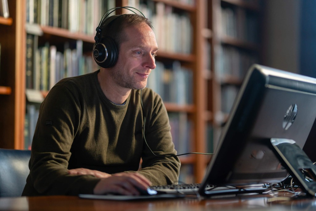 Archivist wearing headphones while reviewing digitised video content at a computer in a library archive